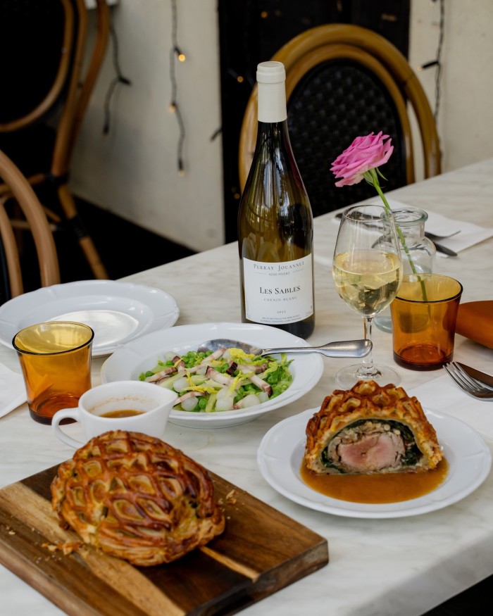 Veal fillet en croûte with petit pois à la française and a bottle of wine on a table at Pique Nique