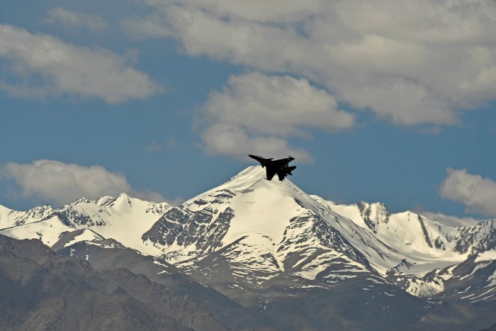 A fighter jet flies over a  mountainous landscape