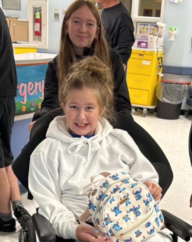 A girl in a wheelchair being pushed by another girl.