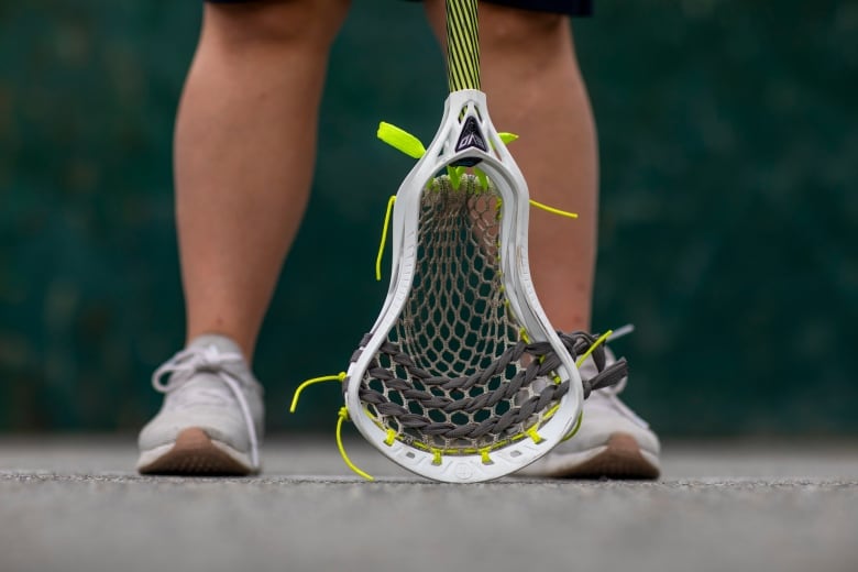 Two legs behind a lacrosse stick.