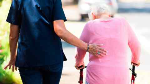 Caregiver helping an elderly woman with her walking aid outdoors