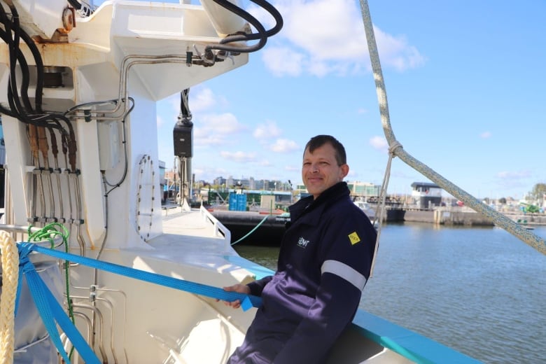 A man leans against the side of a sailboat 