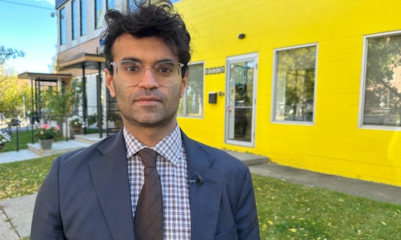 A man in a suit stands outside a yellow building.