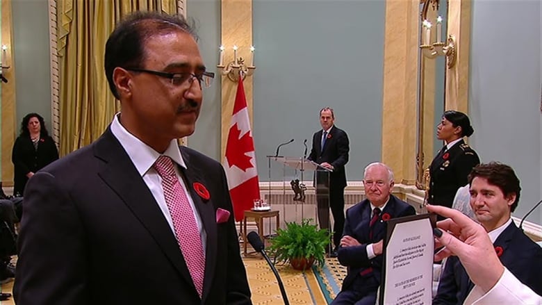 A man with glasses wearing a suit takes a political oath as the prime minister looks on. 