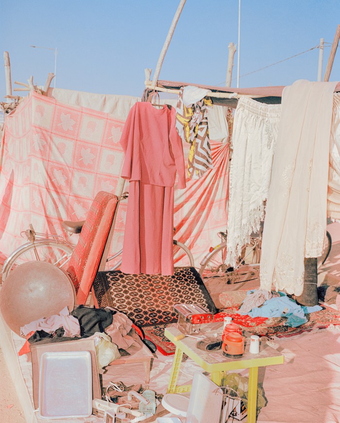 A makeshift outdoor setup featuring a pink outfit hanging from a clothesline next to various household items, including a bicycle, mats, and containers