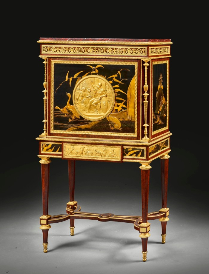 Lavish trunk with four legs, largely made of lacquered wood but very heavily embellished and decorated with what looks like gold leaf or gold paint, including a textured disc on the side with what looks like a gold Roman coin