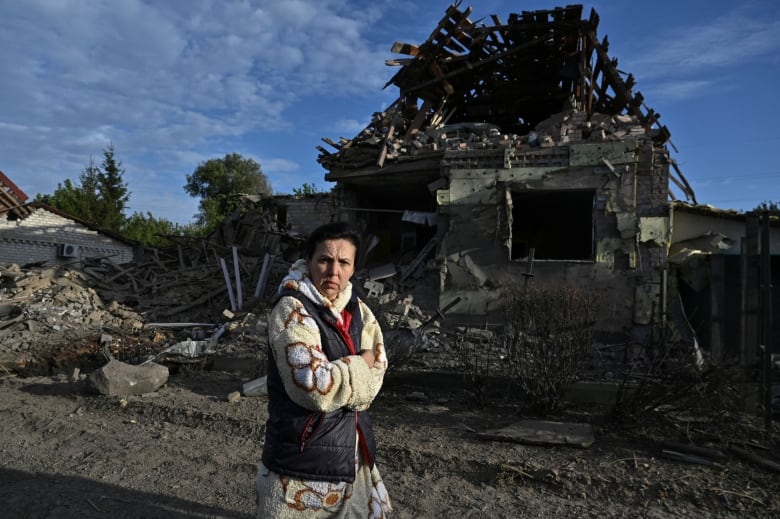 A woman walks next to a heavily damaged house.