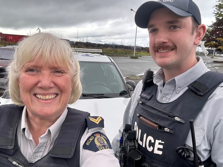 A female and male RCMP officer both smile while in a parking lot.