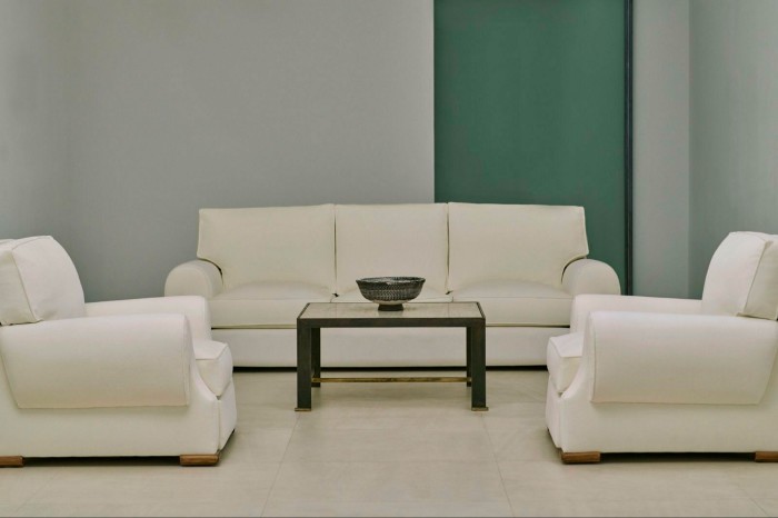 A minimal white sofa and two matching armchairs, arranged around a small wooden table holding an antique-looking bowl