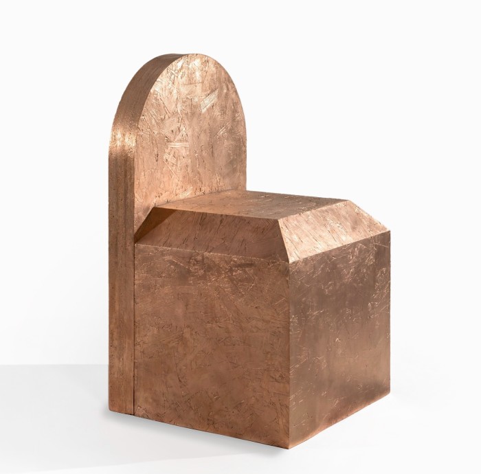 A chunky throne-like shape, cast in bronze, which looks like a cube mounted with a gravestone