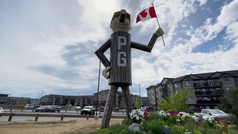 A photo of a wooden lumberjack with apartments behind him.