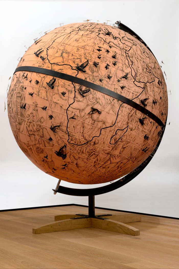 A large globe model of the Earth is studded with small models of birds in flight