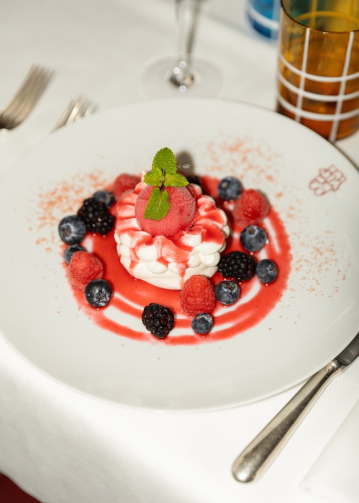 A pavlova in a red sauce and surrounded by blackberries and blueberries