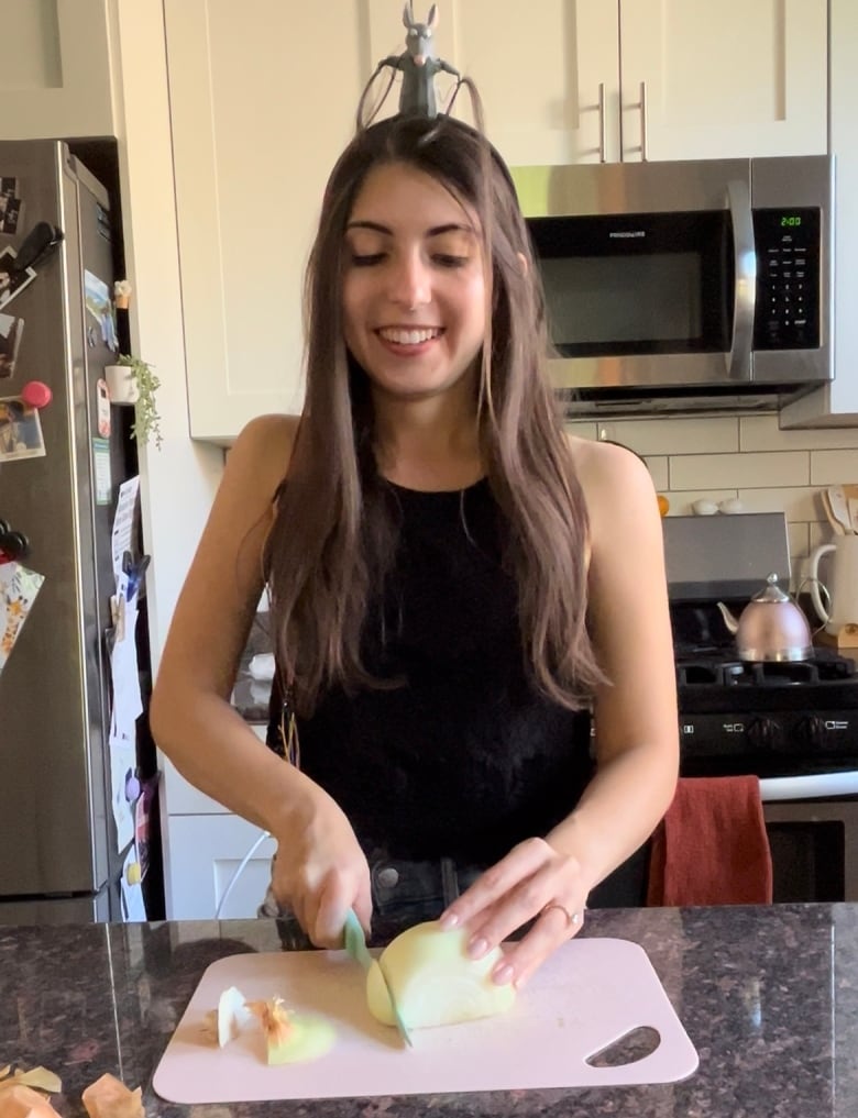 A woman chops an onion while a fake rat sits on her head.