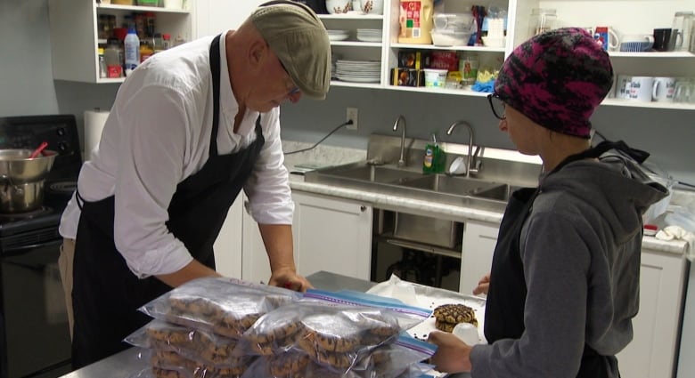 Man and woman in kitchen, putting oat cakes into ziplock bags. 