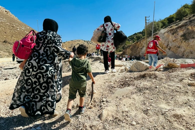 Two women with headcoverings and a small child face away from the camera as they walk on dirt ground.