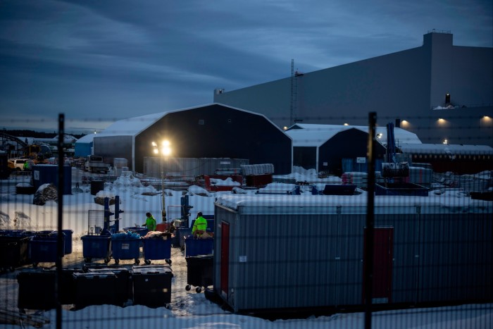 Workers in an outside, snow-covered, yard at the Northvolt gigafactory