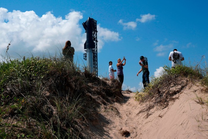 Onlookers watch from nearby sand dunes as SpaceX’s Starship rocket is prepared for a test launch