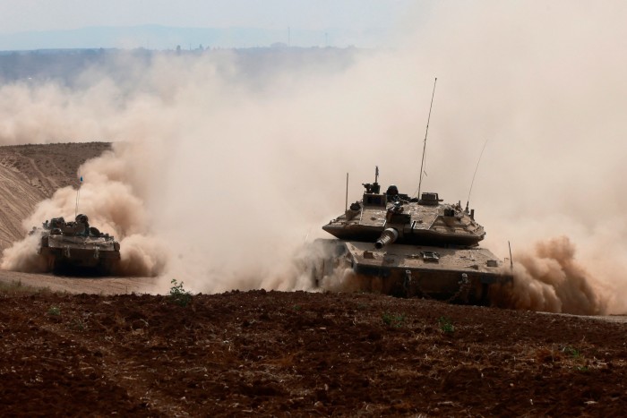 Two tanks drive through clouds of dust as they advance across sandy territory