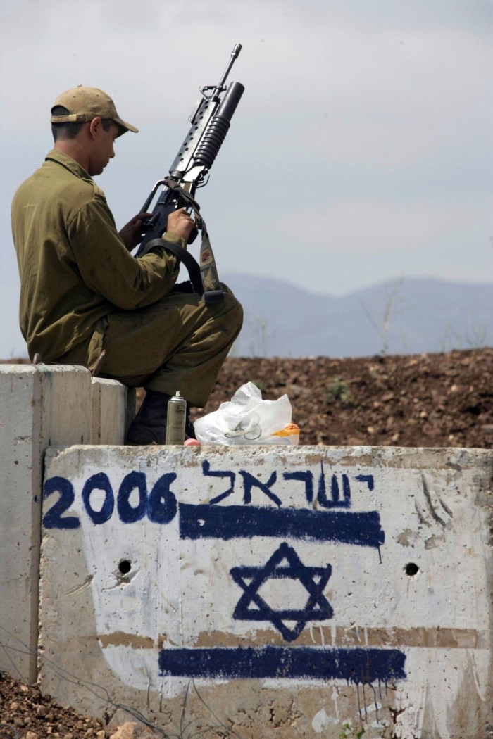 A soldier sits holding a rife on concrete block painted with the Star of David