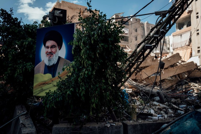 A large banner of a smiling grey-haired man with a beard next to some bushes, damaged buildings and what looks like a fallen crane