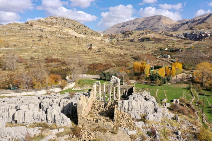 The ruins of an ancient temple and, beyond it, a range of slopes with crops planted on them 