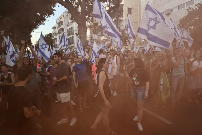 A street crowded with mostly young people, many waving Israeli flags