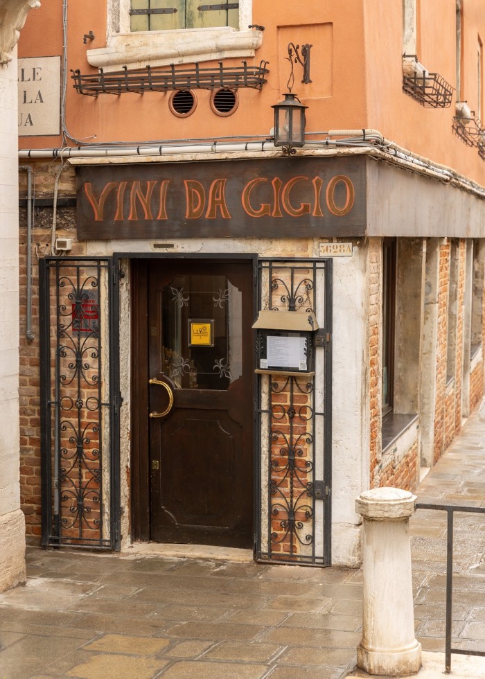 The facade of Vini da Gigio restaurant, in a pink-orange-hued corner building 