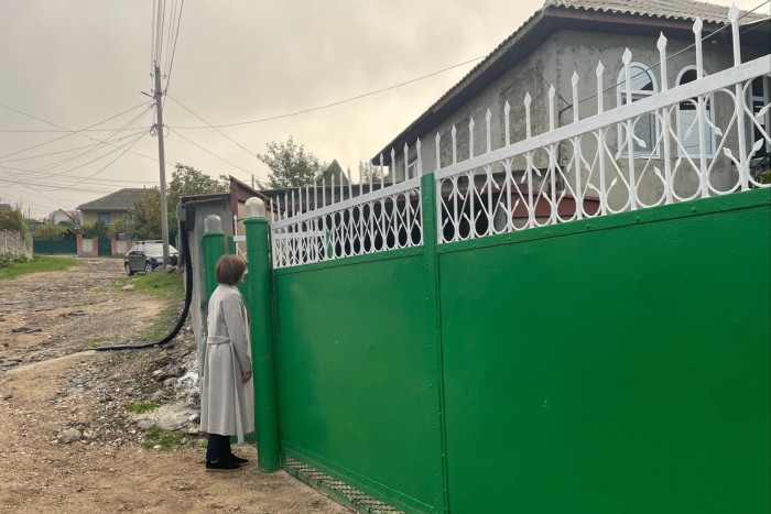 Maia Sandu stands on a dirt road, peering over a tall green fence topped with white decorative metalwork. 