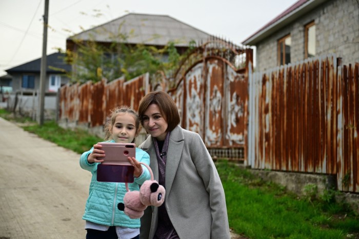 Maia Sandu poses for a selfie with a local child in Bardar. They stand on a quiet street lined with rustic fences and houses.