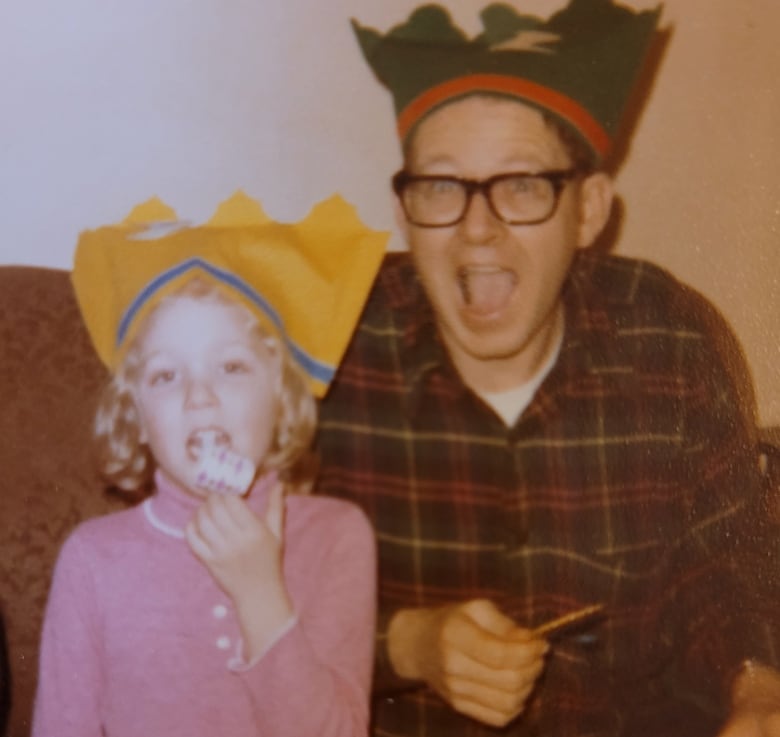 A little girl and a man wearing glasses, both wearing silly hats, pose for a photo. 