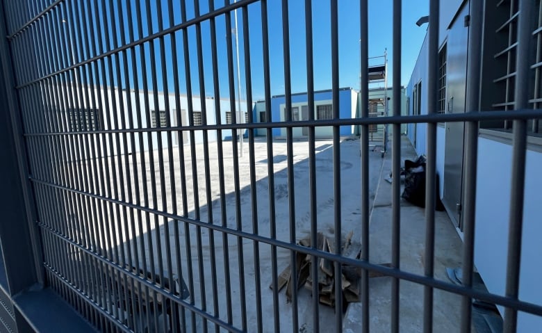 Buildings are shown on the other side of a high fence made of steel bars.