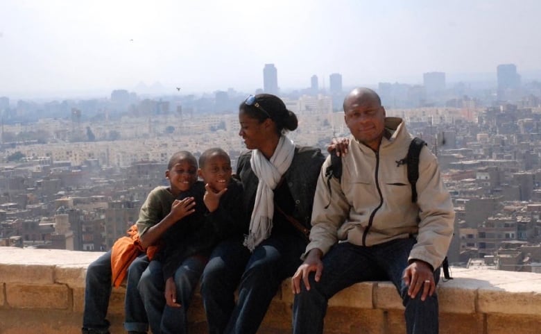 A family of four poses for a photo on a wall overlooking a city.