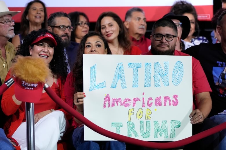 People dressed in red Trump paraphernalia hold a sign than says "Latino Americans for Trump"