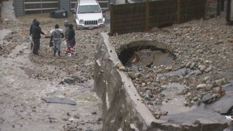 Water flowing down a street like a river with three people navigating their way in the middle. 