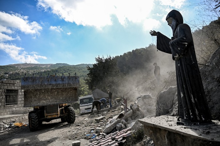 A Statue of the 19th-century Maronite Christian saint Mar Charbel is pictured as a bulldozer moves to clear rubble and debris from the site of a previous Israeli air strike on the village of Aito in northern Lebanon on October 15