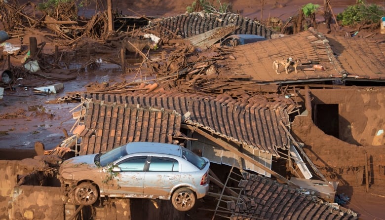 A scene of devastation, rubble covered in brown. A dirty car is visible at the bottom of the image, propped on more rubble. 