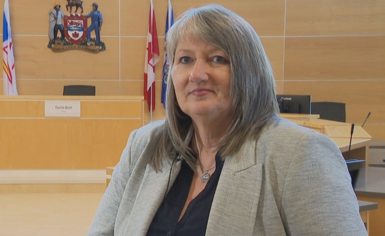 Woman in grey blazer stands in front of desks.