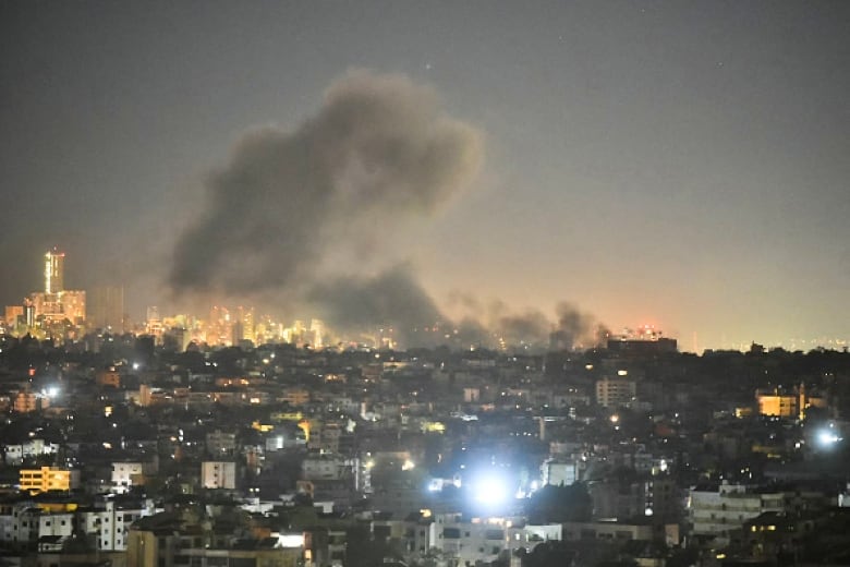 Black smoke billows from buildings at night across an urban landscape.