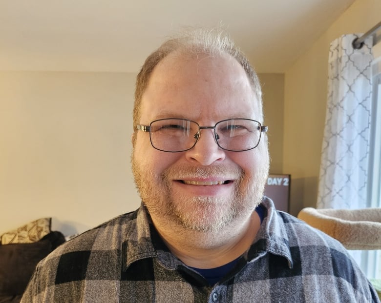 A smiling man with glasses, a beard and a flannel shirt