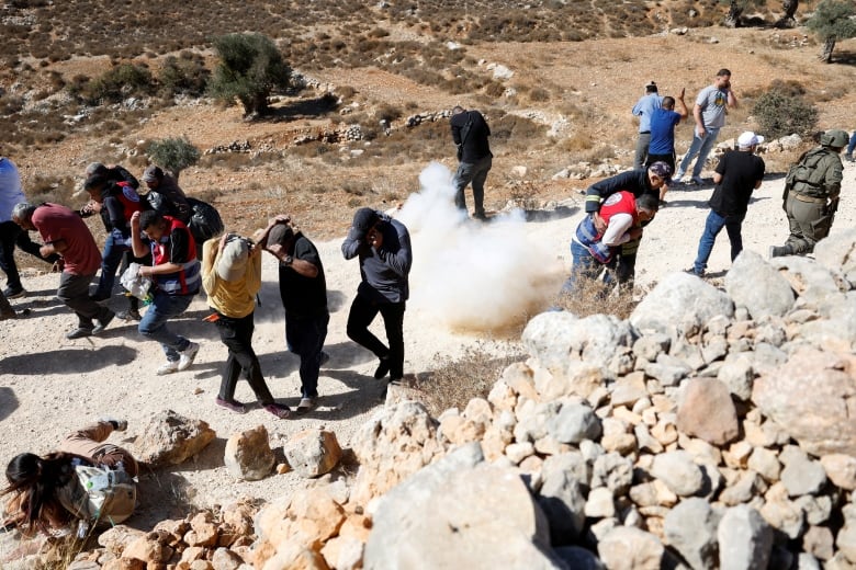 Palestinians run for cover from a stun grenade as Israeli troops deny access to farmers to harvest olives, in Burqa near Ramallah in the Israeli-occupied West Bank October 20, 2024.  