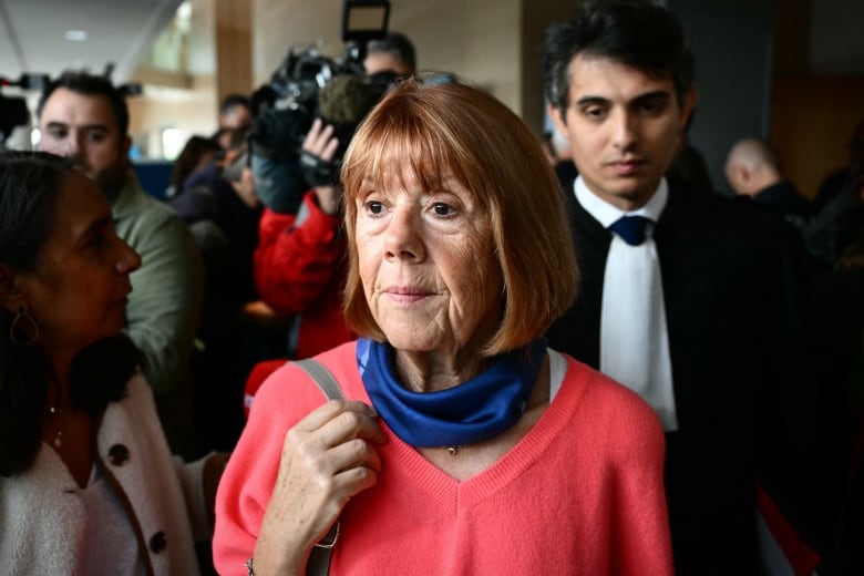 An older woman in a red sweater stands in a crowd