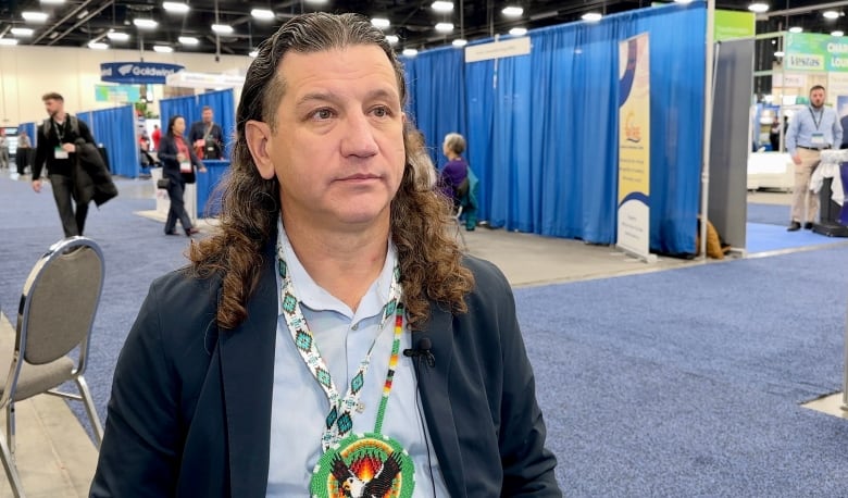 A man is interviewed at an electricity conference with trade show booths in the background.