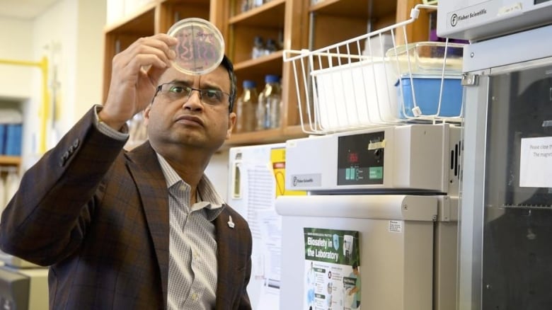 Man holds up petri dish and looks at it