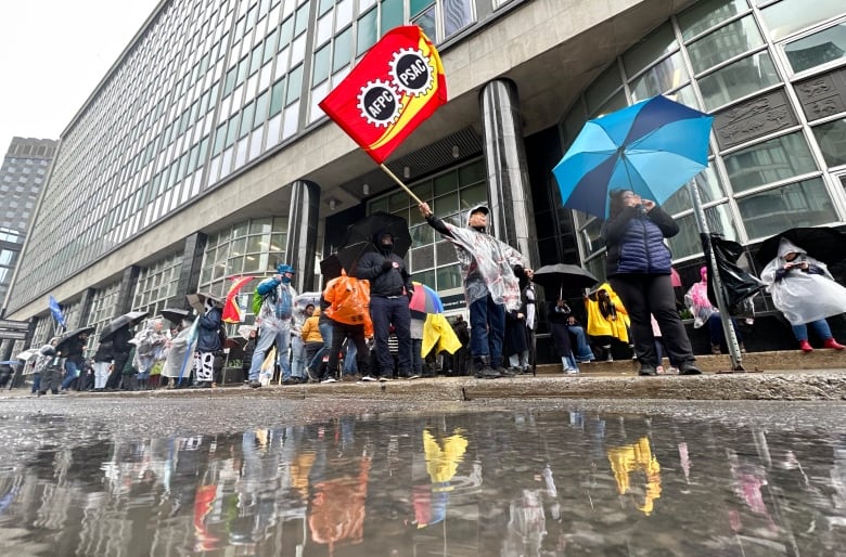 A photo taken at ground level shows a man waving a flag on a street and also the reflection of the street in a puddle. 