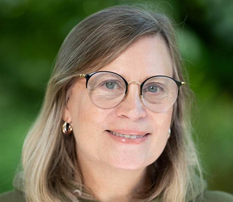 A woman with glasses and blond short hair is smiling at the camera. 