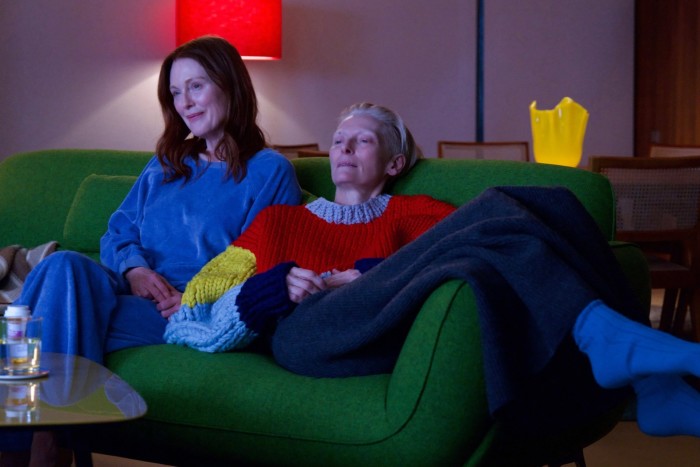 In a stylishly and colourfully furnished room, two women sit on a sofa, smiling