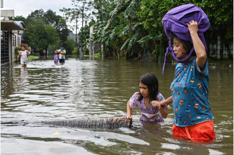 People wade through a street that flooded by heavy rains in Rizal province, east of Manila