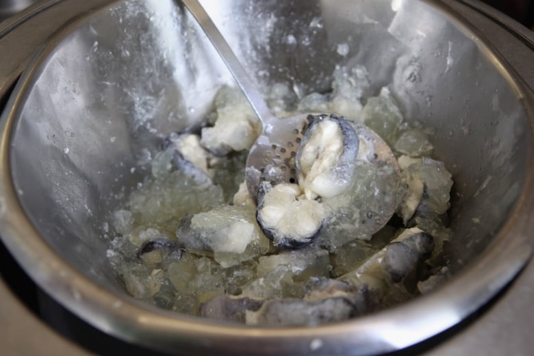 Someone scoops gelatinous grey slices of jellied eels from a silver mixing bowl with a spoon.