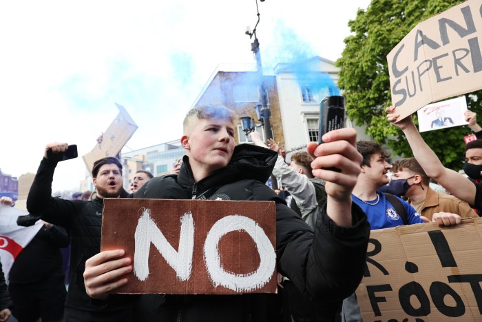 A football fan at the front of a protest holds a lit flare and a sign saying ‘No’ 